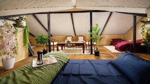 A tented room with a bed, a table with chairs, and potted plants.