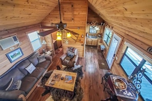 Ein Urlauberhaus-Interieur mit Holzbalkendecke, Deckenventilator, einer Couch, einem Couchtisch, einem Esstisch und einer Küchenzeile.