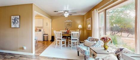 A room with a ceiling fan, a dining area with a table and chairs, and a sofa with a view of the outdoors.