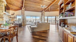 A spacious living area with a stone fireplace, wooden ceiling, and a large window offering a view of the landscape.