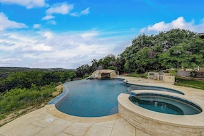 A swimming pool with a curved design, surrounded by a landscaped garden and a view of the landscape.