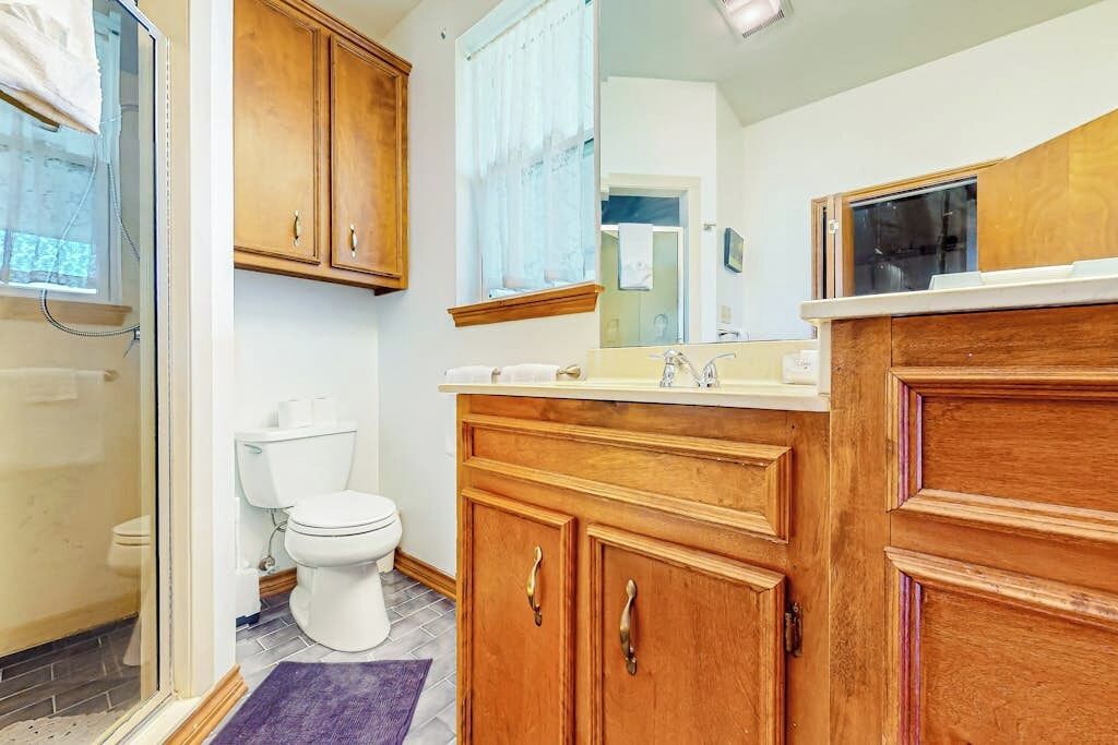 A bathroom with wooden cabinets, a toilet, a shower, and a mirror.