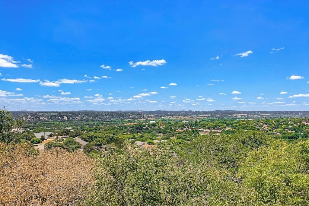 A landscape with a clear sky, distant buildings, and dense vegetation.