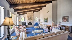 A spacious living room with a fireplace, floral furniture, and a stone wall. - Snowbird-friendly house with game room, full kitchen, balcony, & W/D (Kerrville)