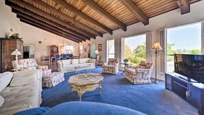 A spacious living room with a high wooden ceiling, a television, and a large window offering a view of the outdoors. - Snowbird-friendly house with game room, full kitchen, balcony, & W/D (Kerrville)