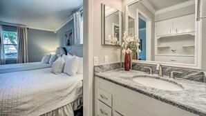 A bedroom with a large bed, a bathroom with a marble sink and double mirrors, and a vase of flowers. - Snowbird-friendly house with game room, full kitchen, balcony, & W/D (Kerrville)