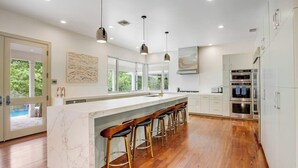 A modern kitchen with a marble island, wooden bar stools, stainless steel appliances, and pendant lighting. - Inviting waterfront home with pool, patio, fireplace, W/D, & dog-friendly (Hunt)