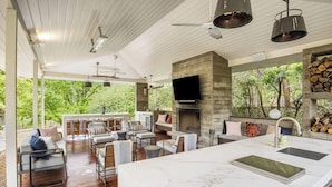 A spacious living area with a large kitchen island, a fireplace, and a TV mounted on a stone wall. - Inviting waterfront home with pool, patio, fireplace, W/D, & dog-friendly (Hunt)