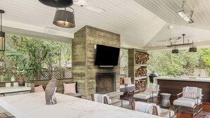 A spacious living area with a large marble island, a fireplace, and a flat-screen TV mounted on a stone wall. - Inviting waterfront home with pool, patio, fireplace, W/D, & dog-friendly (Hunt)