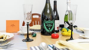 Ein Esstisch mit einer Champagnerflasche, zwei Gläsern, einer Obstschale, einer kleinen roten Frucht, einem Dekorationsgegenstand und einer Schachtel.