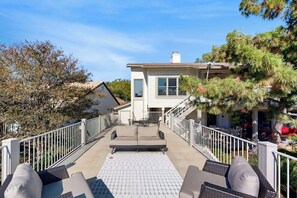Une terrasse couverte avec des meubles d’extérieur, un escalier menant à une maison et des arbres environnants.