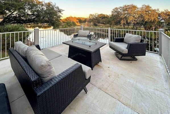 Une terrasse extérieure aménagée avec des meubles en osier, une table à plateau de verre et une vue sur un lac.