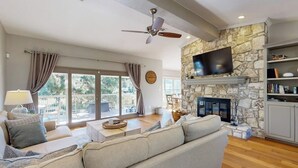 A living room with a stone fireplace, a flat-screen TV, a ceiling fan, and a large window with curtains. - Waterfront, dog-friendly home with lake views, private boat dock (Horseshoe Bay)