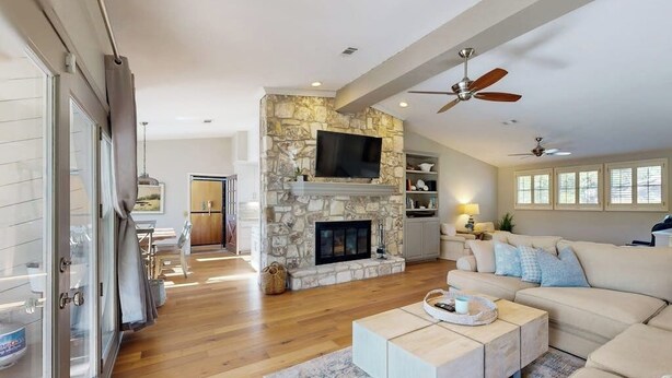 A modern living room with a stone fireplace, a flat-screen TV, a ceiling fan, and a large window. - Waterfront, dog-friendly home with lake views, private boat dock (Horseshoe Bay)