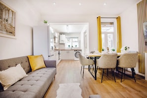 Ein modernes Wohnzimmer mit einer Couch, einem Esstisch, Stühlen und einer Küche im Hintergrund.