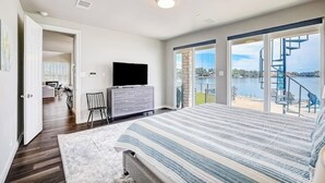 Un dormitorio con una cama grande, televisión, cómoda y vistas a un balcón con piscina y escaleras.