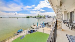 Un balcón con vistas a un lago, una piscina y una terraza con sillas y sombrillas.