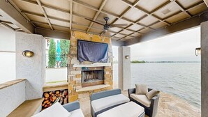 An outdoor seating area with wicker furniture, a stone fireplace, and a view of the water. - Luxe lakefront retreat with private pool, spa, lakeside terrace, gourmet kitchen (Horseshoe Bay)