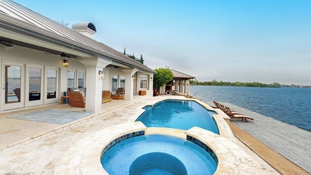 A pool area with a view of the water, a covered patio, and a building with large windows. - Luxe lakefront retreat with private pool, spa, lakeside terrace, gourmet kitchen (Horseshoe Bay)
