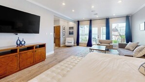 A modern hotel room with a large bed, a TV, a wooden entertainment unit, a sofa, and a dining area. - Luxe lakefront retreat with private pool, spa, lakeside terrace, gourmet kitchen (Horseshoe Bay)