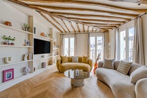 Ein Wohnzimmer mit einer Couch, einem Glastisch und einem Fernseher an einer weißen Wand.