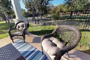 Terrassenmöbel aus Rattan mit Kissen, einer Streifenmatte und einem umzäunten Bereich mit Bäumen.