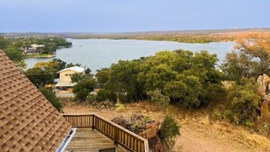 Une terrasse en bois donnant sur un lac, entourée d’arbres, avec une vue lointaine sur des maisons.