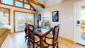 Un espace repas avec une table en verre et des chaises en bois, un mur en pierre et une vue dégagée grâce à de grandes fenêtres.