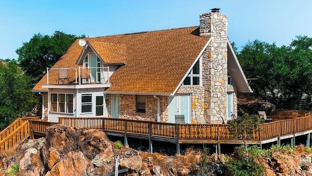 Une maison en pierre à deux étages, dotée d’une terrasse en bois et d’une cheminée en pierre.
