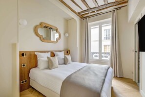 Ein Schlafzimmer mit einem Holzkopfende, einem großen Spiegel, einem Bett mit weißen Leinen und Blick auf einen Balkon durch ein Fenster.