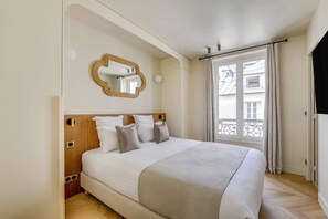 Ein Hotelzimmer mit einem großen Bett, einem Holzkopfteil, einem Spiegel und einem Fenster mit Blick auf Gebäude.