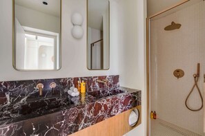 Ein Badezimmer mit Marmorwaschtisch, einem Spiegel und einer Duschkabine.