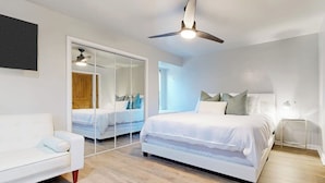 Une chambre moderne avec un grand lit, un canapé blanc, un ventilateur de plafond et une armoire avec un miroir.