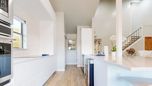 Une cuisine moderne avec des meubles blancs, un plancher en bois et une vue sur le salon.