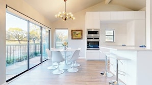 Une cuisine moderne avec des meubles blancs, un coin repas avec des chaises blanches et une grande fenêtre donnant sur un balcon.