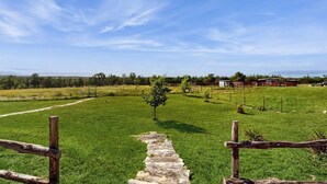 A rural landscape with a stone pathway leading through a green field, wooden fence posts, and distant farm buildings. - Idyllic home with fire pit, gazebo, patio, & amazing deck views - dog-friendly (Fredericksburg)