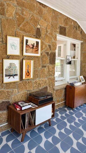 Une pièce avec un mur en pierre, une fenêtre avec des volets blancs, un meuble en bois et une platine vinyle.