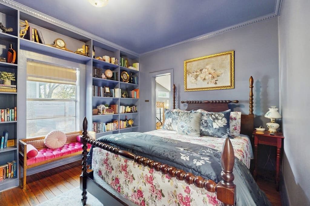 A bedroom with a large bookshelf, a bed with floral bedding, and a painting on the wall.