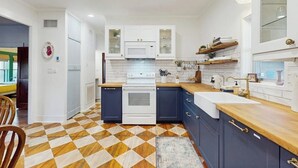 Eine moderne Küche mit weißen Schränken, einer Mikrowelle und einem Herd. Der Holzboden weist ein geometrisches Muster auf.