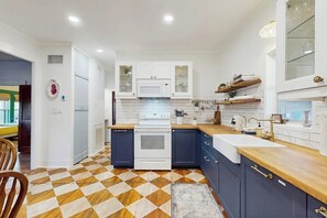 Eine moderne Küche mit weißen Schränken, einer Mikrowelle und einem Herd. Der Holzboden weist ein geometrisches Muster auf.