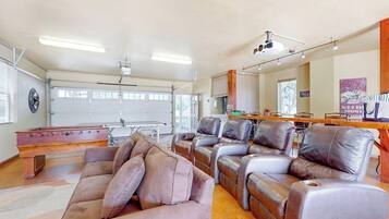 A spacious living room with a pool table, leather recliners, and a garage door.