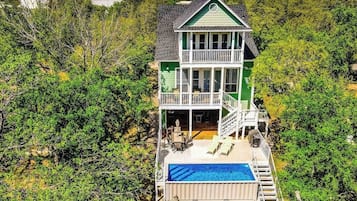 A two-story house with a balcony, a swimming pool, and a forested backdrop.