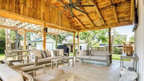 An outdoor covered patio with wooden furniture, a ceiling fan, and a stone sculpture. - Historic home a block from Main St with hot tub, sauna, fast WiFi & firepit (Fredericksburg)