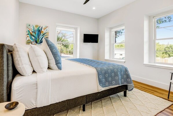 Un dormitorio con cama, almohadas, una colcha, televisión y ventanas.