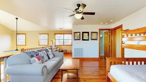 Une pièce avec un plancher en bois, un canapé, un lit, un ventilateur de plafond et des tableaux encadrés accrochés au mur.