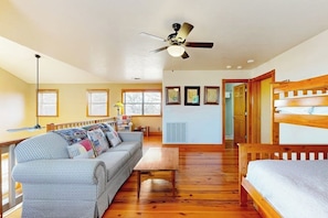 A room with a wooden floor, a sofa, a bed, a ceiling fan, and framed pictures on the wall. - Peaceful home with fire pit, gazebo, patio, & amazing deck views - dog-friendly (Fredericksburg)