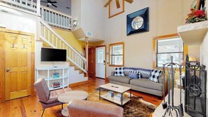 Un salon spacieux avec un escalier, une cheminée, un téléviseur et un coin salon confortable.