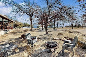 An outdoor seating area with chairs and a grill, surrounded by trees and a building. - Peaceful home with fire pit, gazebo, patio, & amazing deck views - dog-friendly (Fredericksburg)