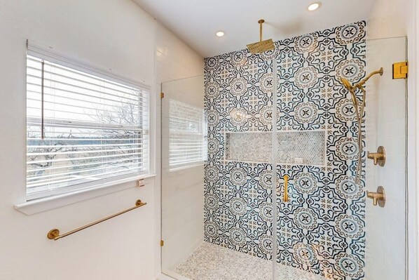 A bathroom with patterned tiles, a window with blinds, and a towel rack.