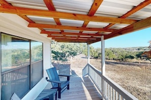 A covered outdoor area with wooden beams, a bench, and a view of a vineyard.